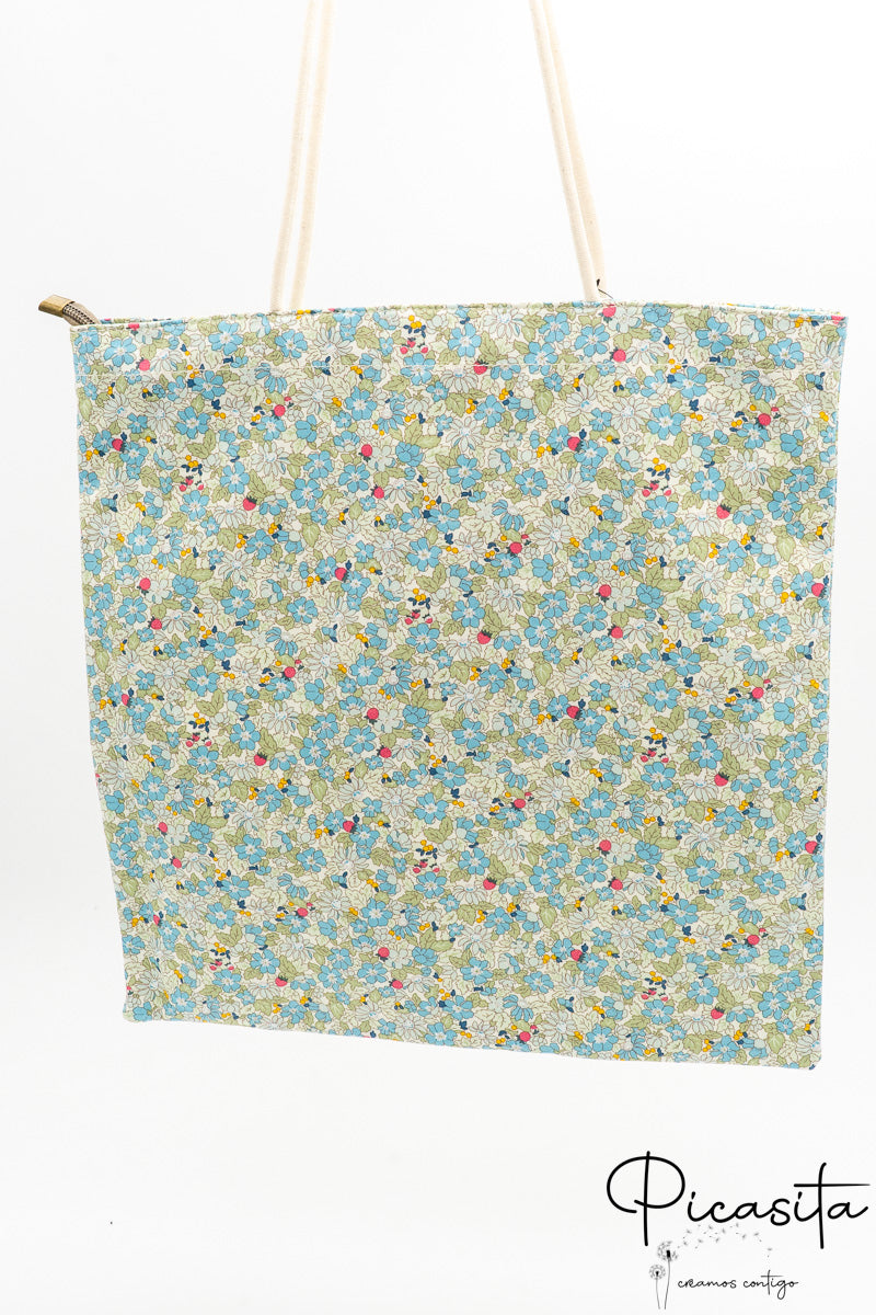 Bolsa tote con estampado de flores verdes y blancas colgada verticalmente mostrando su capacidad.