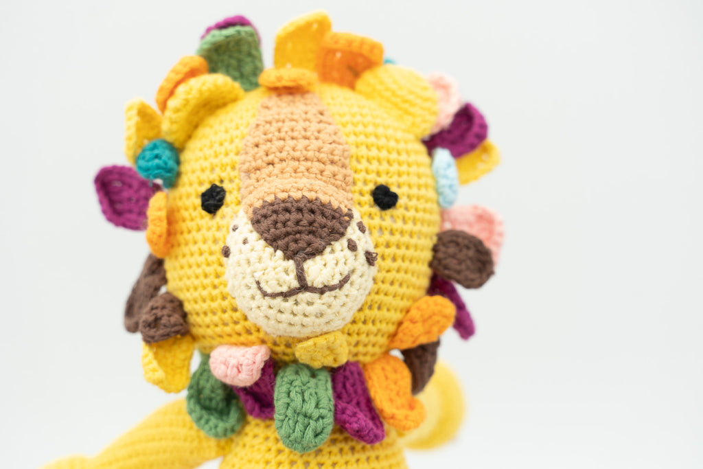 Primer plano de la cara de un león de crochet amarillo con melena de pétalos coloridos.