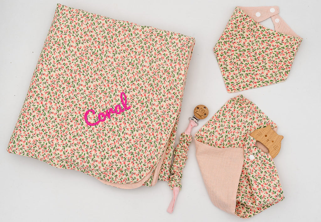Set rosa con copertina a fiori e il nome Coral ricamato, bavaglino a bandana, mussola rosa con massaggiagengive in legno e catenella portaciuccio.
