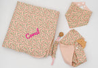 Set rosa con copertina a fiori e il nome Coral ricamato, bavaglino a bandana, mussola rosa con massaggiagengive in legno e catenella portaciuccio.