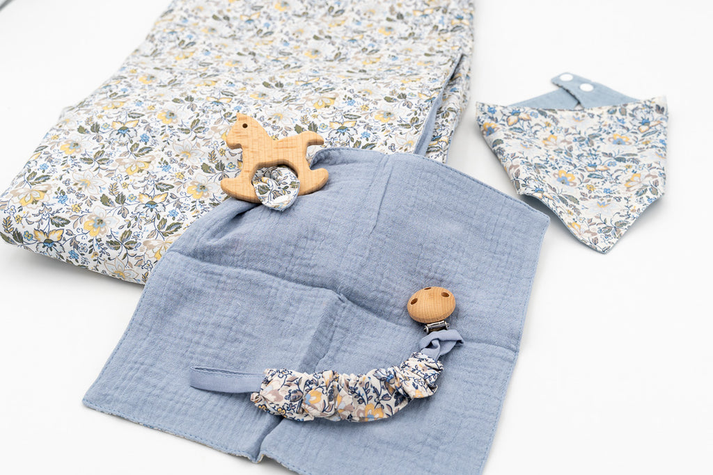 Set blu con copertina a fiori, bavaglino a bandana, mussola blu con massaggiagengive a cavallino in legno e catenella portaciuccio con clip in legno.