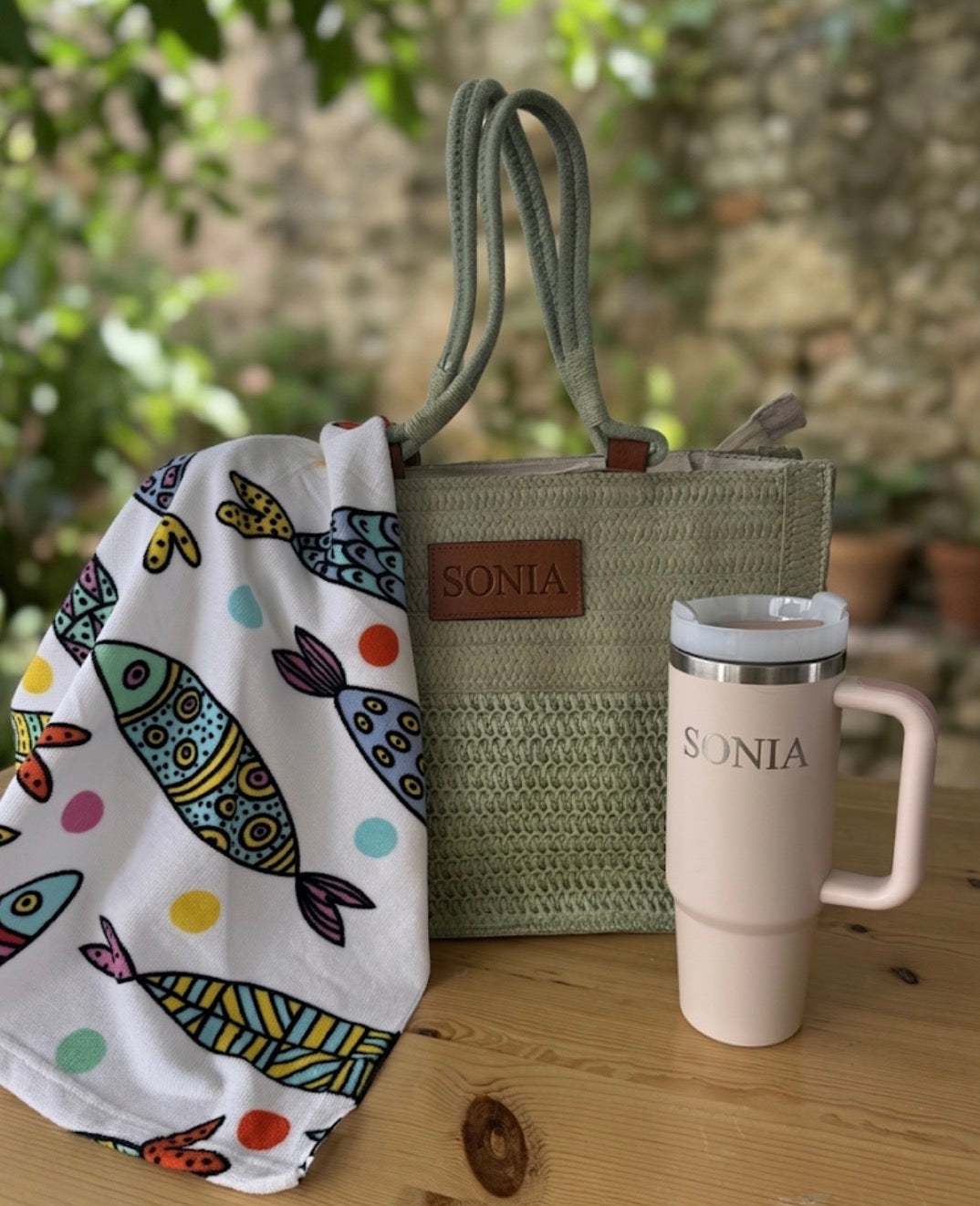 Bolso de rafia verde con nombre Sonia grabado y toalla blanca con estampado de peces.