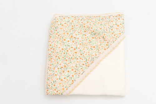 Copertina per neonato color senape piegata, con il cappuccio stampato a fiori e il pizzo coordinato.