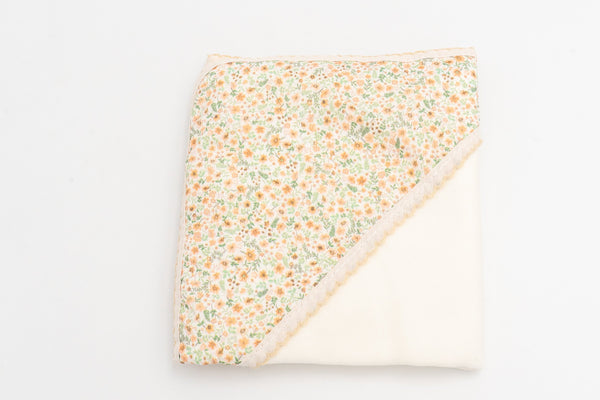 Copertina per neonato color senape piegata, con il cappuccio stampato a fiori e il pizzo coordinato.
