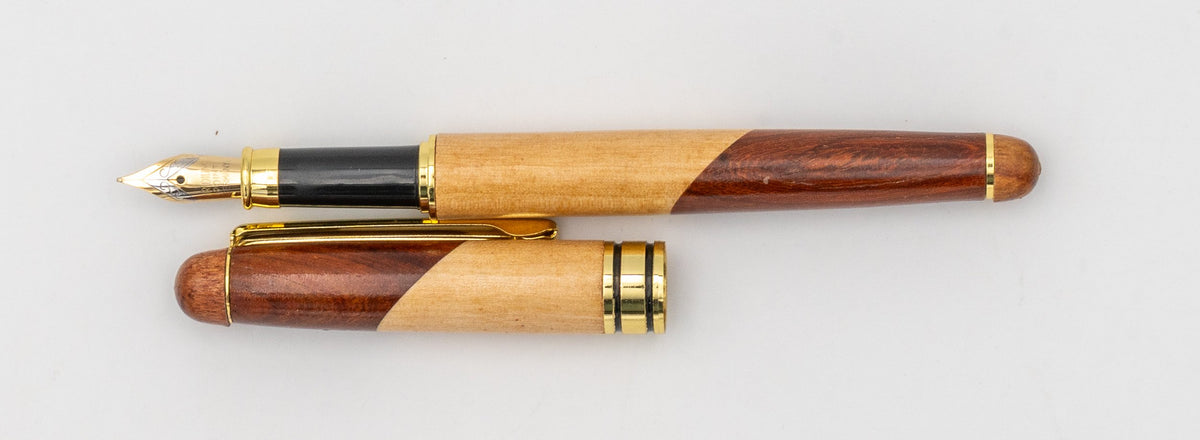 Penna stilografica in legno bicolore con cappuccio rimosso e pennino visibile.