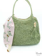 Bolso hobo verde oliva trenzado con borla de conchas marinas y pañuelo geométrico rosa.