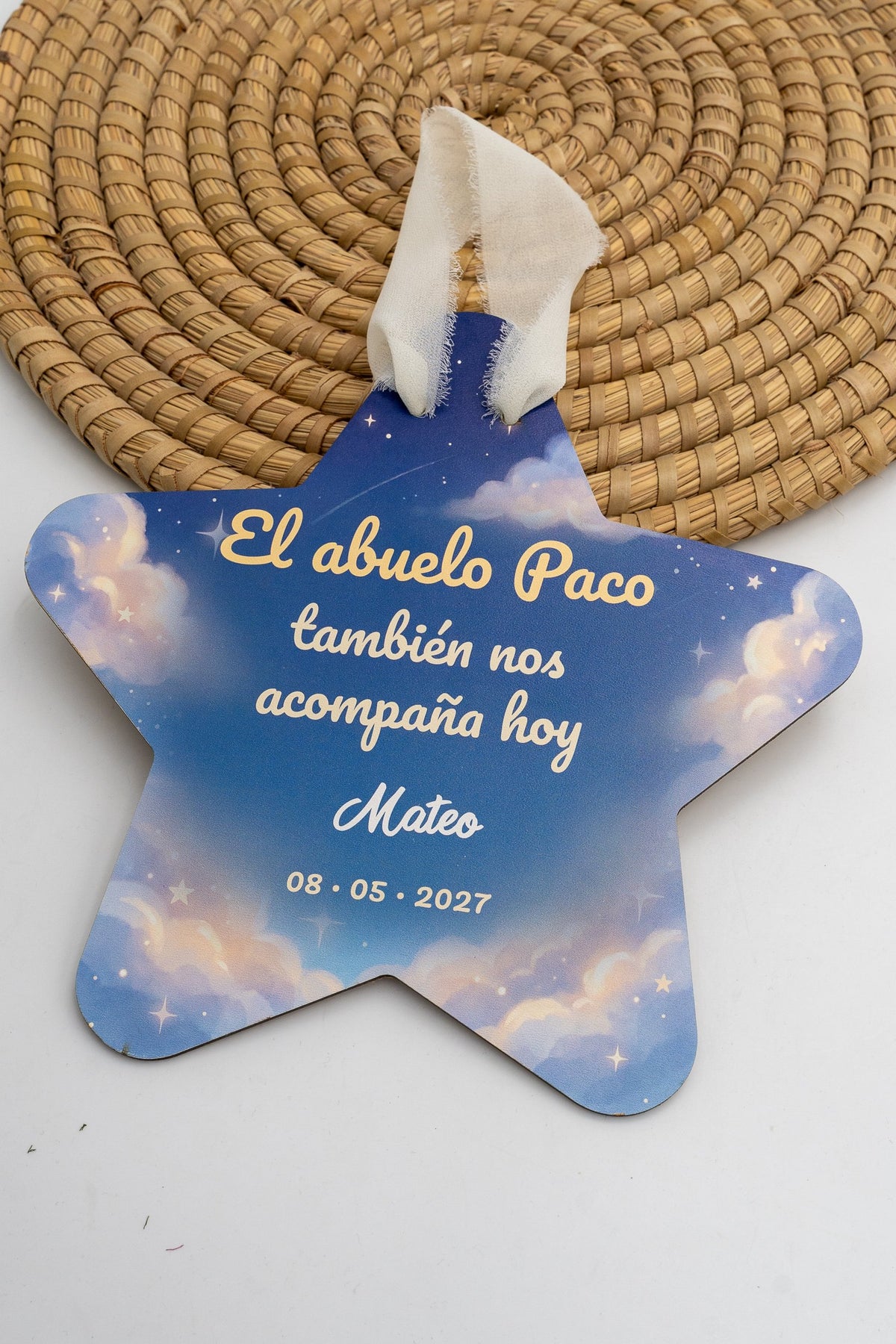 Stella per la comunione con sfondo di cielo azzurro con nuvole e stelle, la frase «El abuelo Paco también nos acompaña hoy», il nome di esempio Mateo e la data, con nastro color crema.