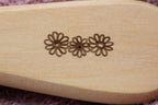 Dettaglio di tre margherite incise nel legno di una spazzola.