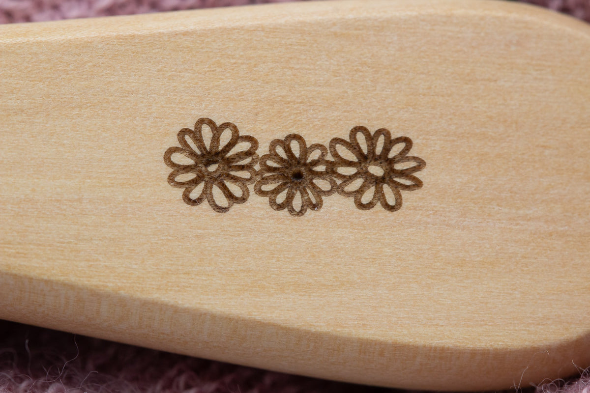 Dettaglio di tre margherite incise nel legno di una spazzola.