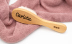 Spazzola in legno con il nome Carlota su un tessuto rosa.