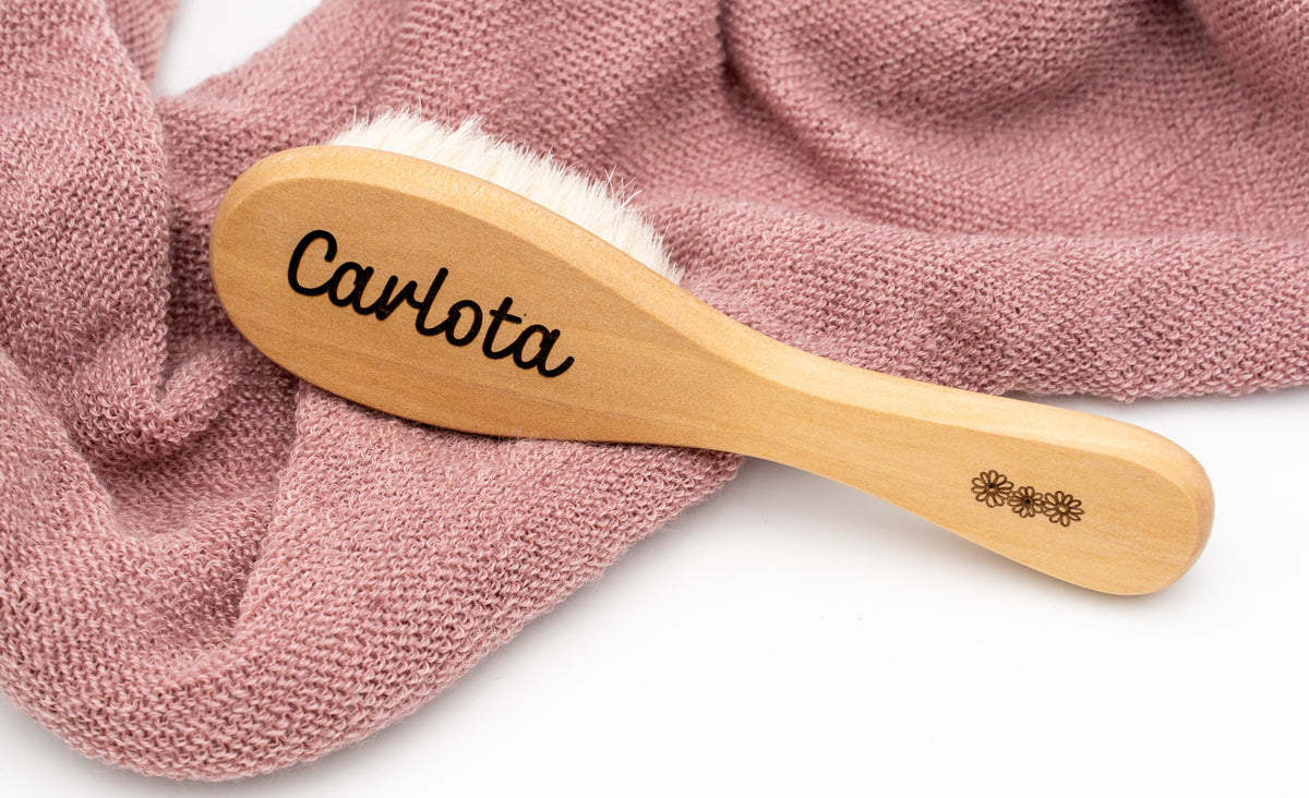Spazzola in legno con il nome Carlota su un tessuto rosa.
