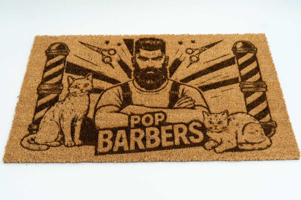 Felpudo con logotipo de barbería incluyendo ilustración de barbero, gatos y postes de barbero.