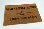 Felpudo con frase original y símbolo de advertencia grabado en fibra natural de coco.