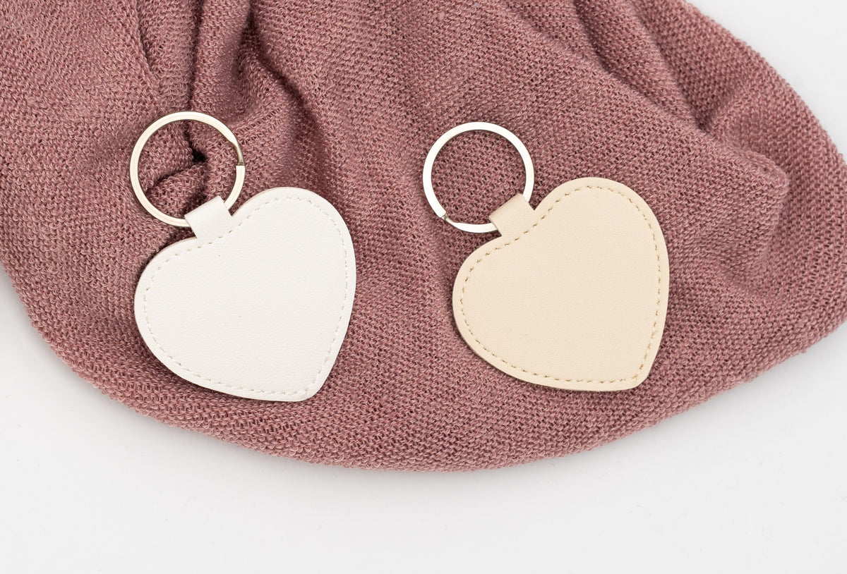 Portachiavi a cuore bianco e beige non personalizzati su tessuto rosa.