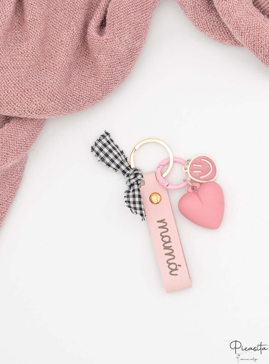 Detalle de la tira de polipiel rosa con grabado mamá y lazo de tela a cuadros.