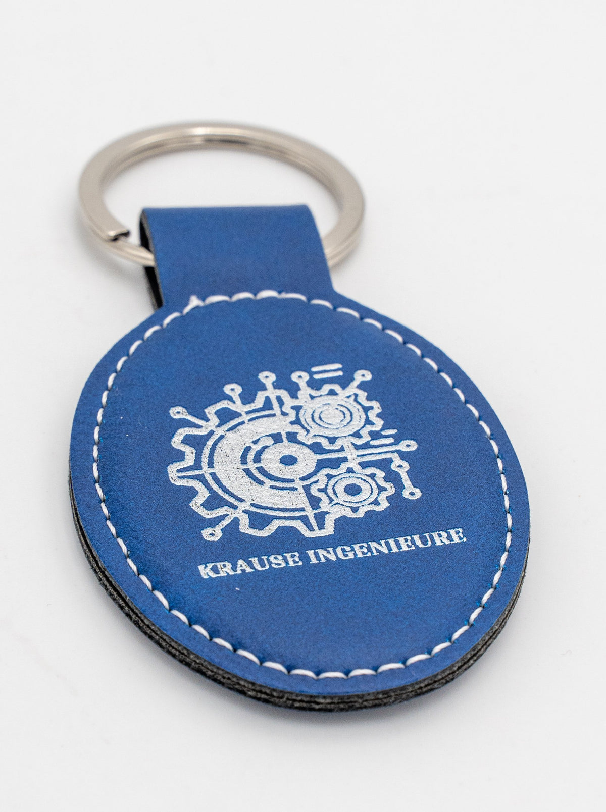 Portachiavi ovale blu con logo chiaro e cucitura bianca.