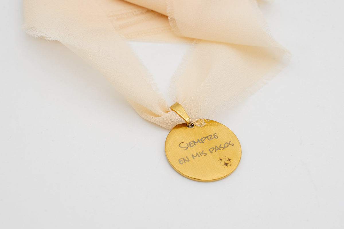 Ciondolo dorato con la frase «Sempre nei miei passi» legato a un nastro di chiffon color pesca