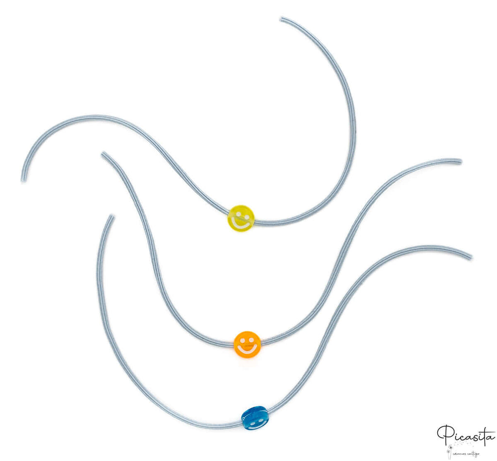 Tres pulseras elásticas grises con cuentas de sonrisas en amarillo, naranja y azul.