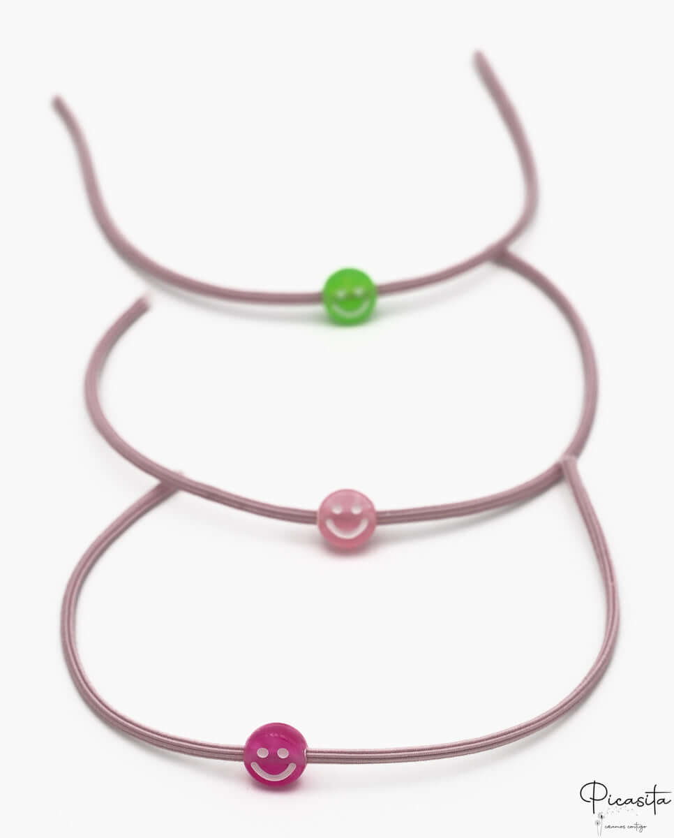 Tres pulseras elásticas malva con cuentas de silicona en forma de sonrisa verde y rosa.