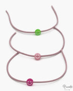 Tres pulseras elásticas malva con cuentas de silicona en forma de sonrisa verde y rosa.