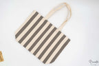Bolso de rayas grises y blancas extendido sobre fondo blanco neutro.