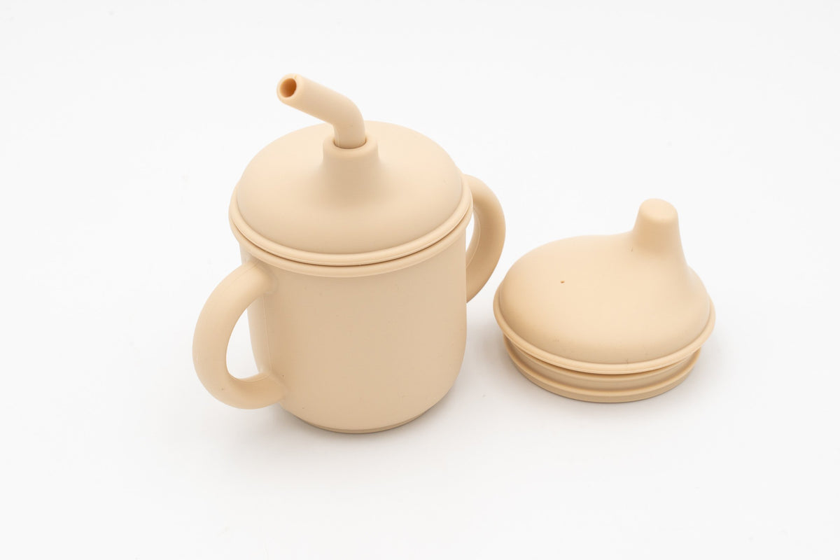 Bicchiere beige per bambini aperto accanto ai due coperchi