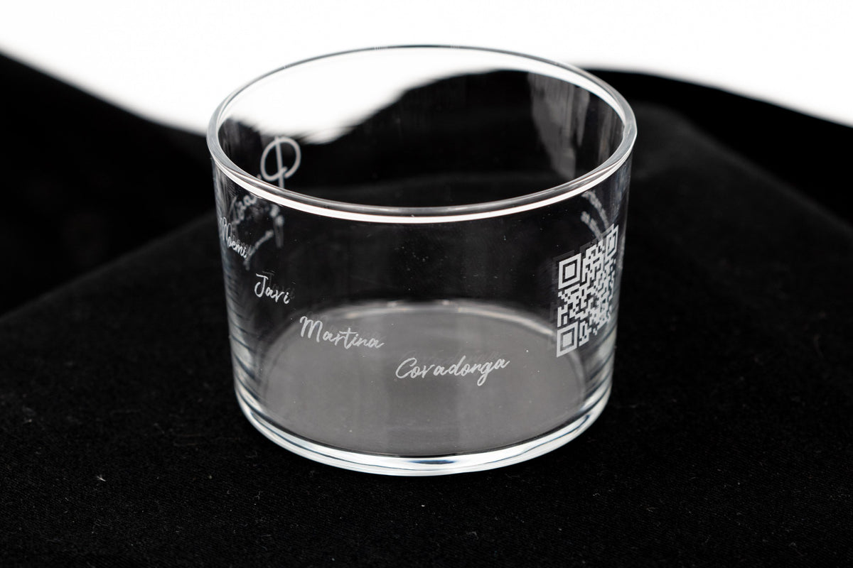 Vaso de cristal transparente con nombres grabados en cursiva sobre una superficie oscura elegante.